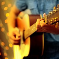 A DSLR photo of a man playing a guitar during a concert. The man is playing an acoustic guitar and wearing a blue shirt, the face is invisible. Some blured lights can be seen at the background.