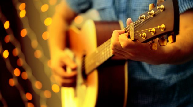 A DSLR photo of a man playing a guitar during a concert. The man is playing an acoustic guitar and wearing a blue shirt, the face is invisible. Some blured lights can be seen at the background.